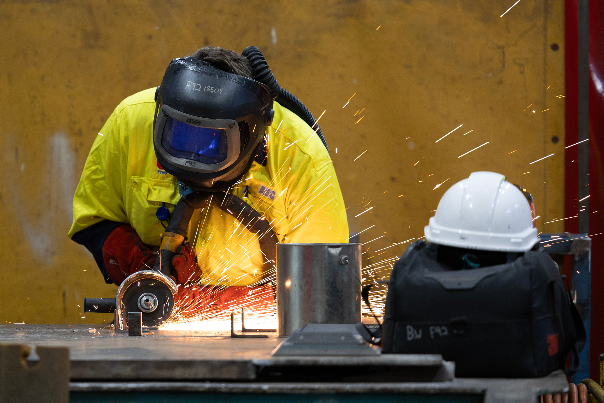 Tradesmen in protective gear using an angle grinder to cut metal sheet.