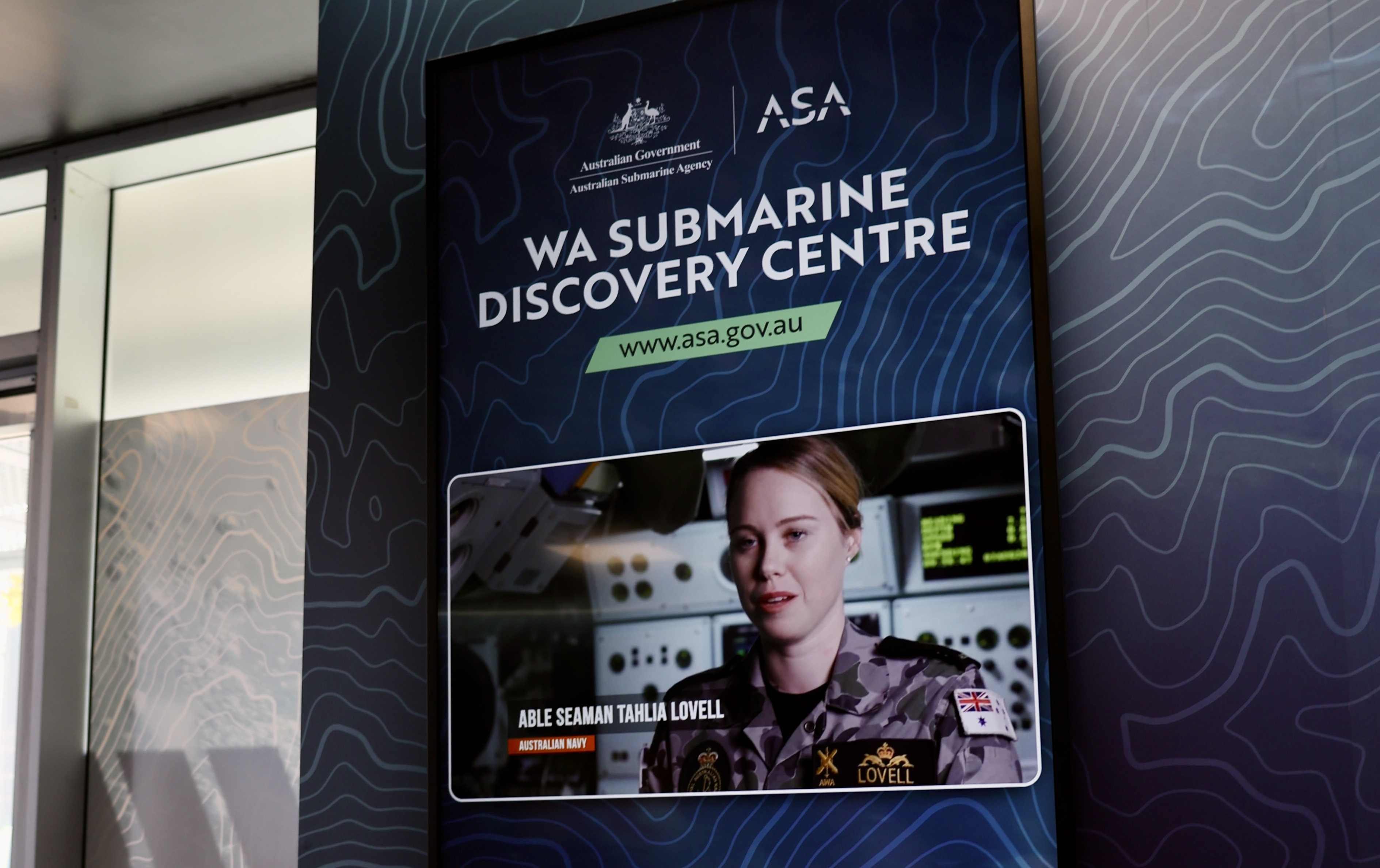 Sign for WA Submarine Discovery Centre with ASA logo and screen showing a navy member in a submarine setting.