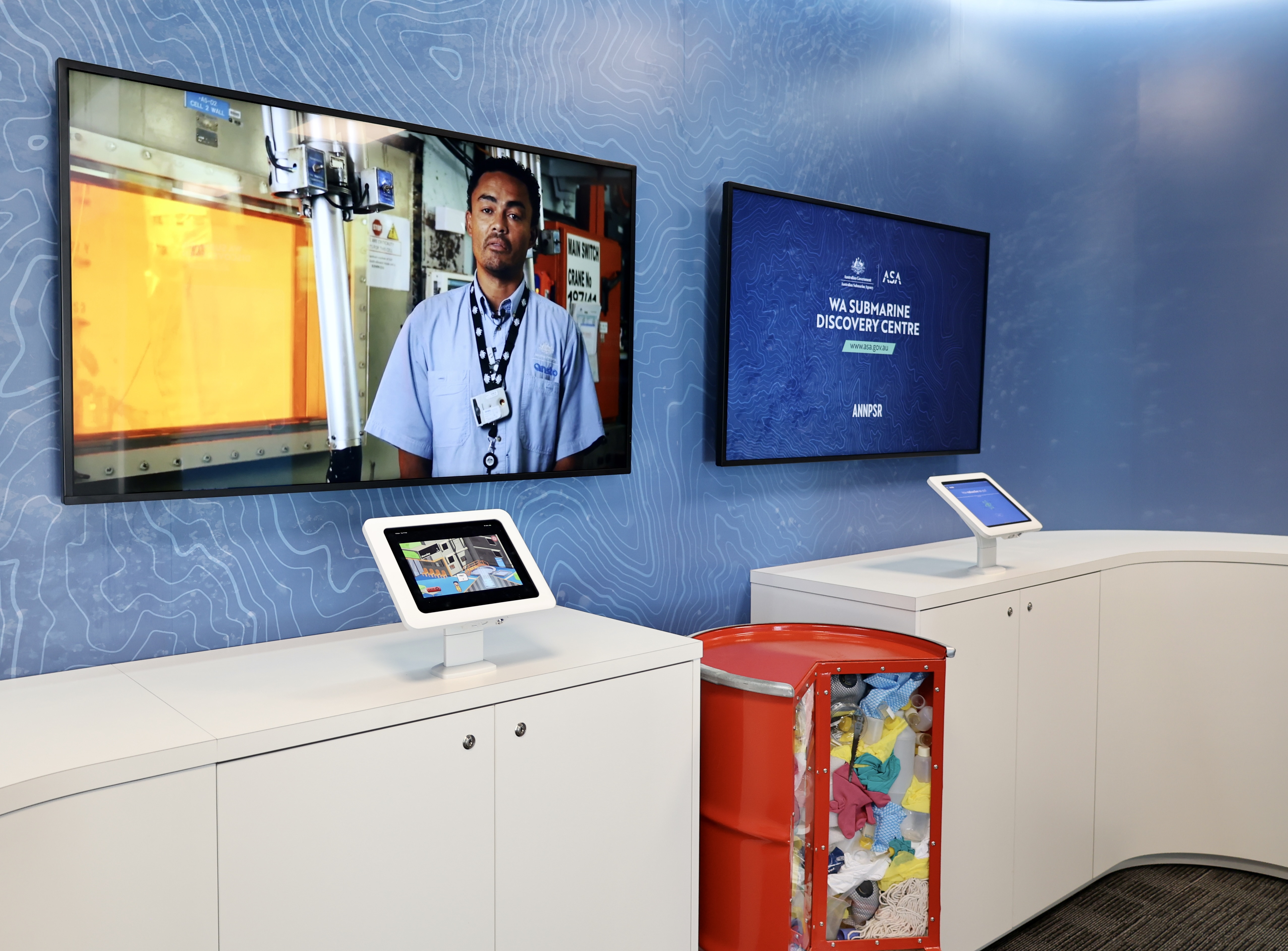 Interactive displays and touch screens at WA Submarine Discovery Centre, with video screens and a red storage unit.