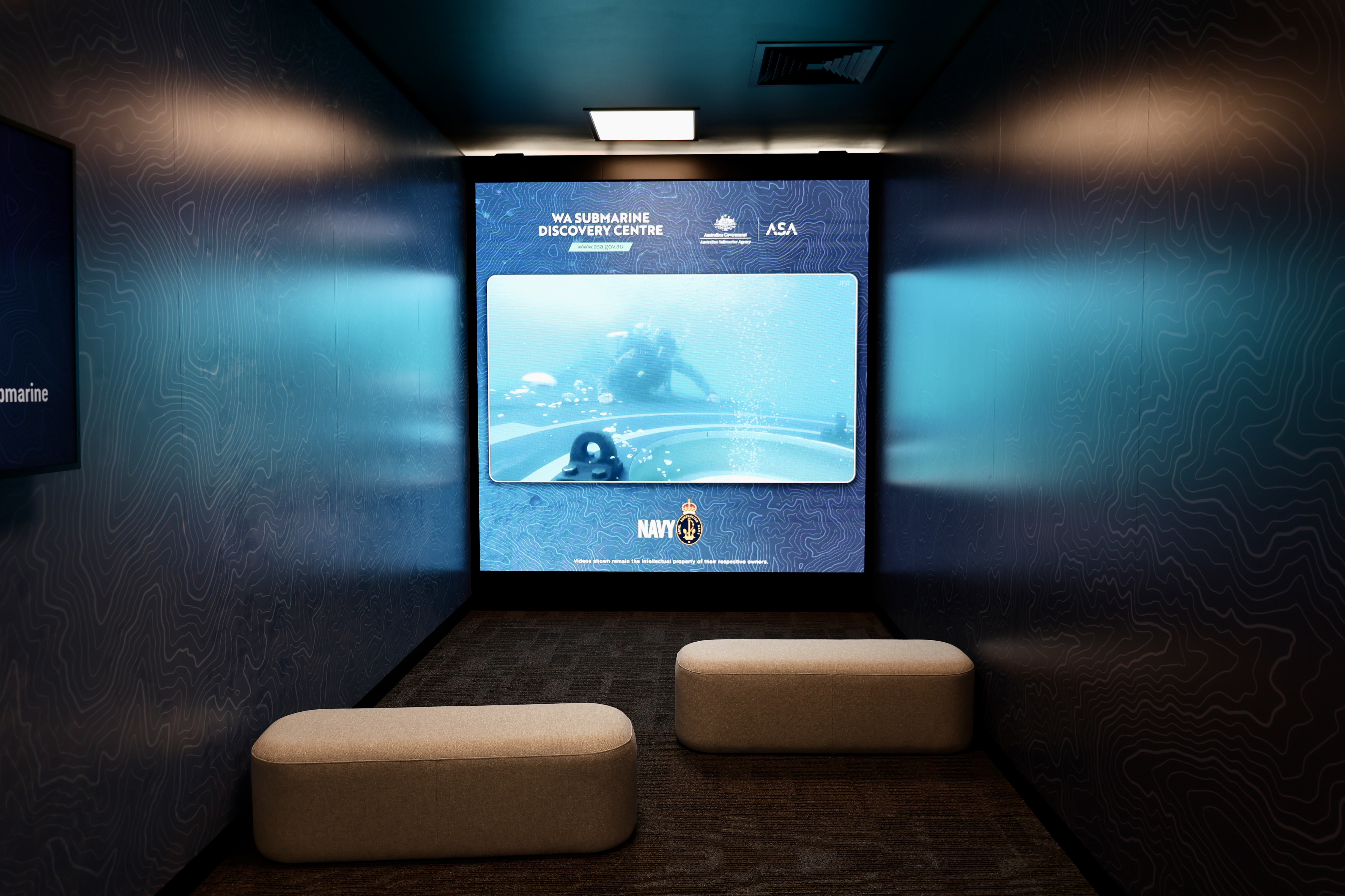 Small theatre room with bench seats and screen showing underwater video at WA Submarine Discovery Centre.