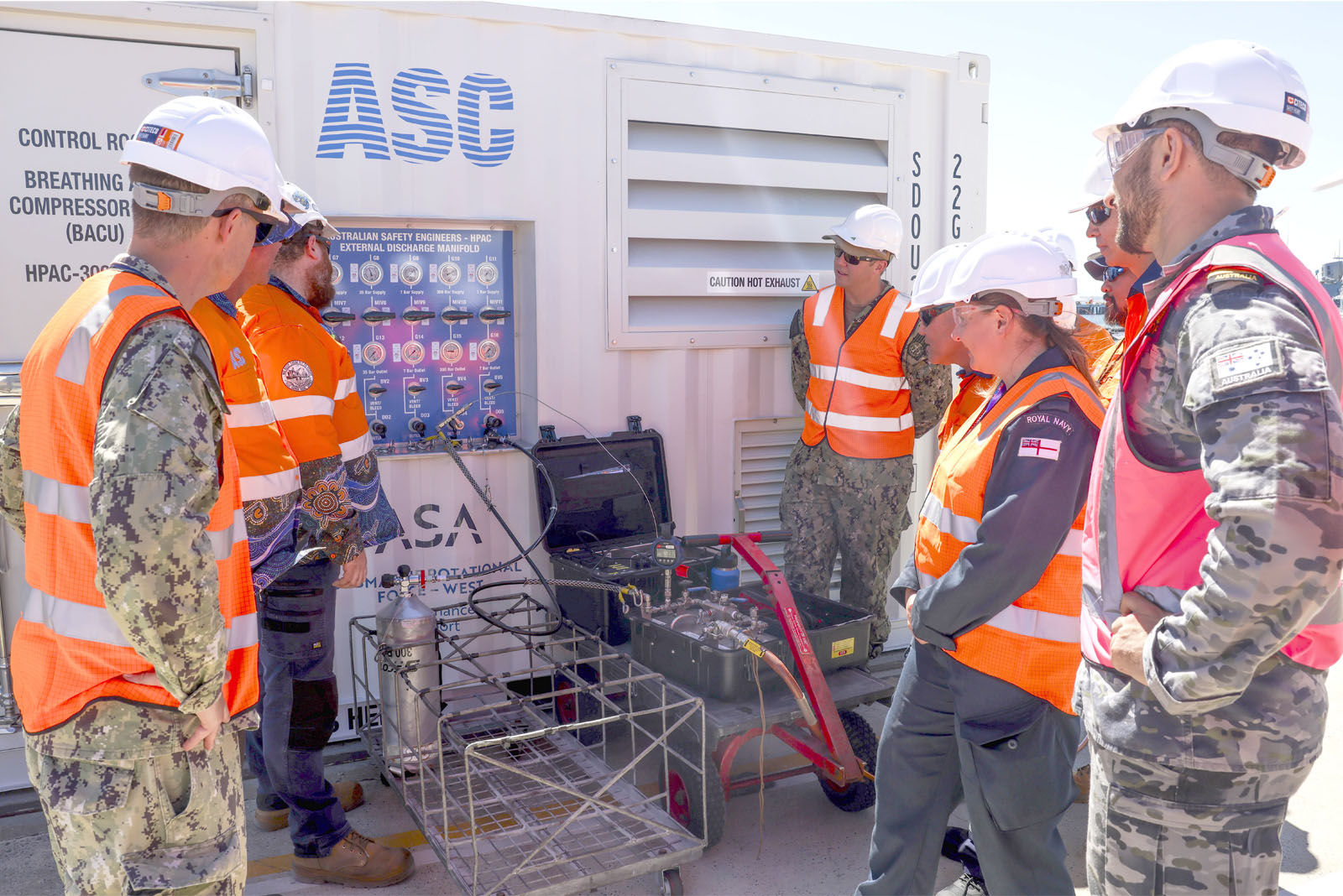 Australian, UK and US personnel and industry representatives inspect the Australian-made High-Pressure Air Compressor that supported submarine sustainment on the Royal Navy’s HMS Anson at HMAS Stirling under AUKUS.  The unit was used to charge Emergency Breathing Device Apparatus tanks, supporting safe submarine operations.  Image by PO Phot Unaisi Luke; © UK MOD Crown Copyright 2026