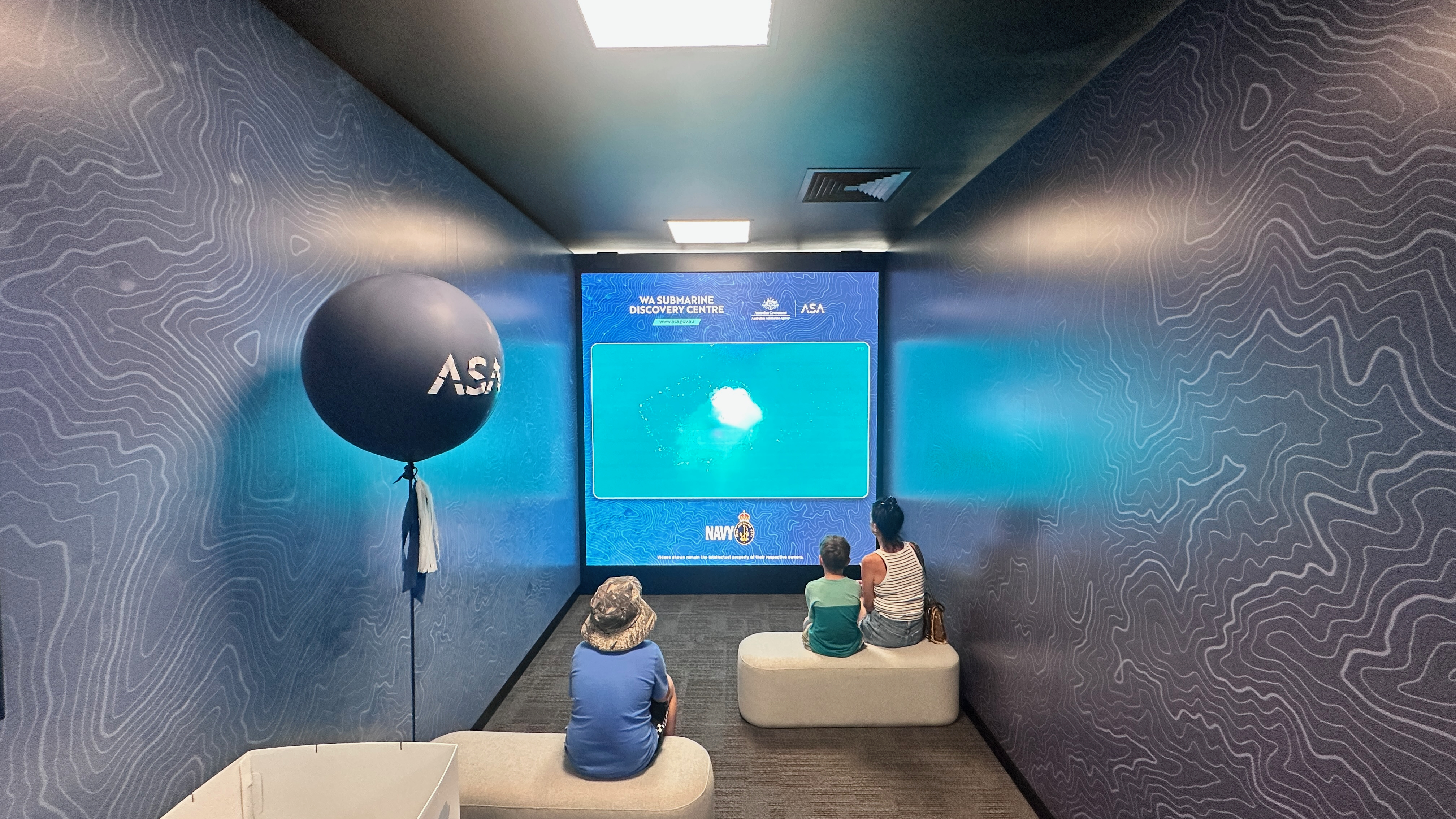 Visitors watch an underwater video on a large screen in a small viewing room at WA Submarine Discovery Centre.