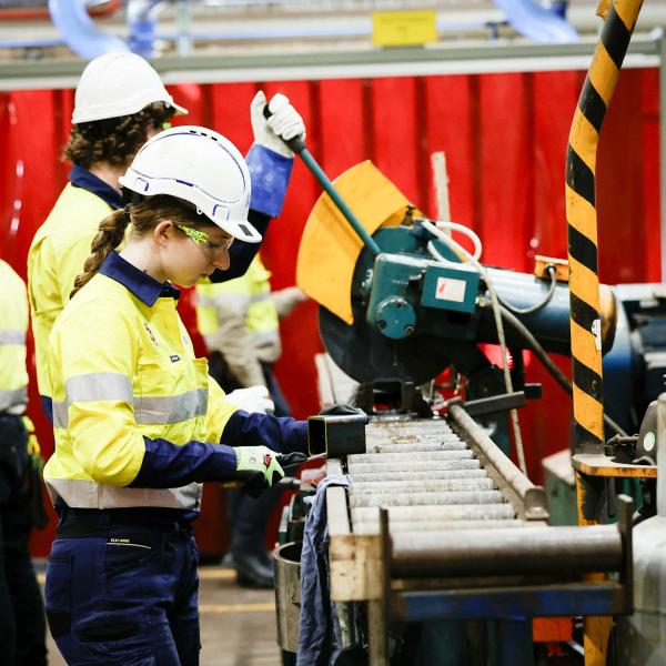People working with heavy factory machinery, wearing high vis clothing.