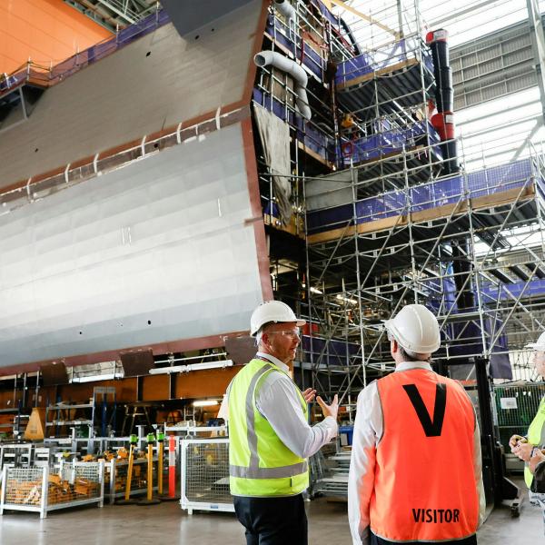 Three people in high-vis vests standing in a warehouse reviewing the construction of submarine parts.