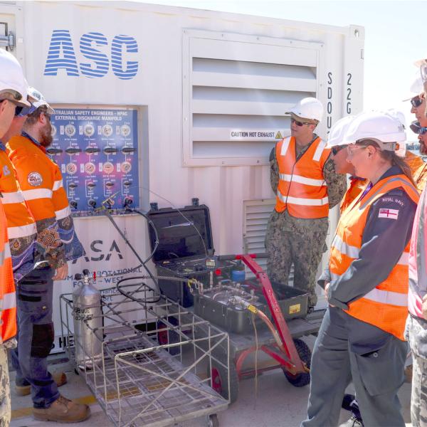 Australian, UK and US personnel and industry representatives inspect the Australian-made High-Pressure Air Compressor that supported submarine sustainment on the Royal Navy’s HMS Anson at HMAS Stirling under AUKUS.  The unit was used to charge Emergency Breathing Device Apparatus tanks, supporting safe submarine operations.  Image by PO Phot Unaisi Luke; © UK MOD Crown Copyright 2026