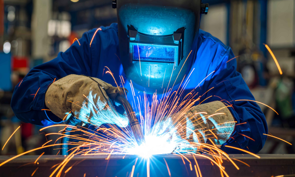 A welder in full protective gear welding a corner joint.