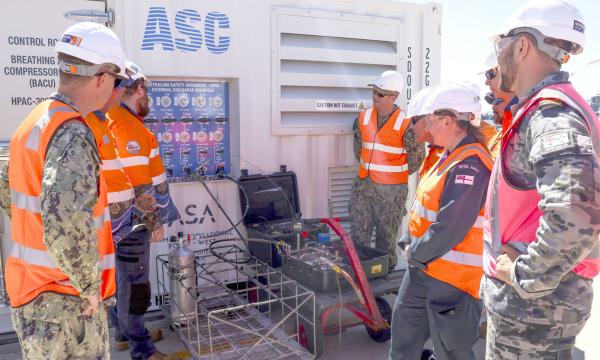 Australian, UK and US personnel and industry representatives inspect the Australian-made High-Pressure Air Compressor that supported submarine sustainment on the Royal Navy’s HMS Anson at HMAS Stirling under AUKUS.  The unit was used to charge Emergency Breathing Device Apparatus tanks, supporting safe submarine operations.  Image by PO Phot Unaisi Luke; © UK MOD Crown Copyright 2026