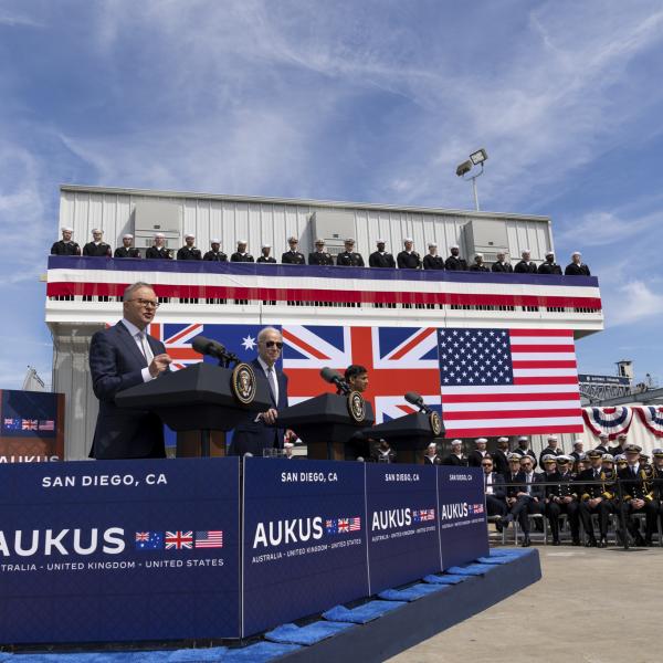 Officials speak at AUKUS event in San Diego, with US, UK and Australian flags and navy crew on a platform behind.